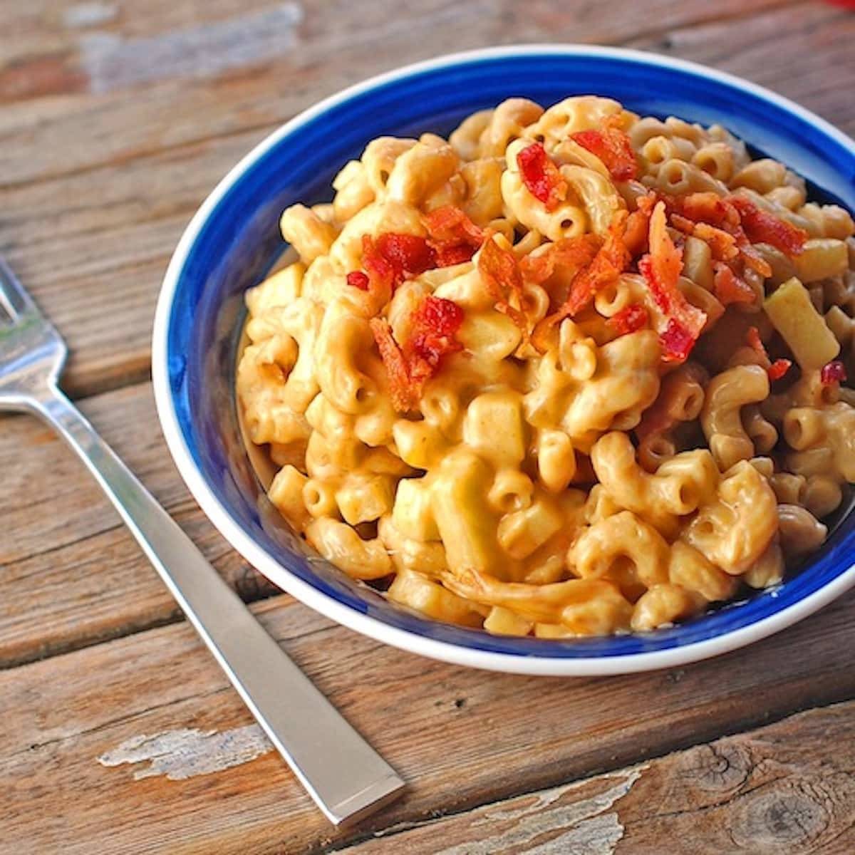 Butternut squash mac and cheese with caramelized onions, crispy bacon, and fresh sweet apples in a blue bowl.